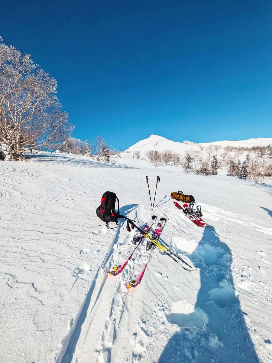 Skis, a splitboard and packs resting in the snow below a sunlit peak