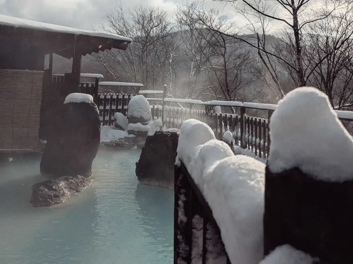 Steam rising from the milky open-air onsen between snow-capped rocks